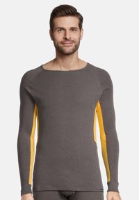 Langærmet skjorte lavet af grå stof med gule mesh accenter i siderne, med rund halsudskæring og tætsiddende design.