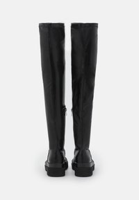 Bottes cuissardes en similicuir noir à la texture lisse, dotées de fermetures éclair sur le côté extérieur et d'une semelle épaisse.