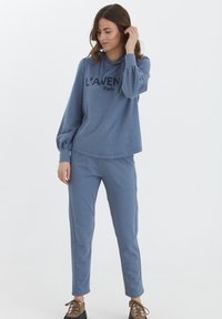 Blå bomullshoodie med texten "L'AVEN Paris", långärmad och i avslappnad passform; matchas med stretchbyxor i samma färg. Bruna snörskor.