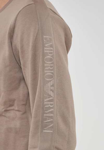 Camicia marrone a maniche lunghe con texture a costine, con il logo "EMPORIO ARMANI" lungo la manica sinistra in una tonalità più chiara.