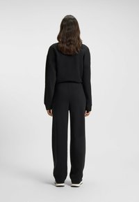 Svart atletisk outfit med en långärmad topp med avslappnad passform och vida byxor. Slät textur med minimalistisk design.