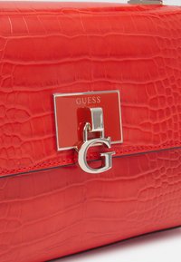 Rote Handtasche aus Kunstleder mit Krokodillederstruktur, ausgestattet mit einem silbernen Verschluss und einem metallischen "G"-Akzent.