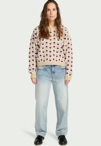 Maglione beige lavorato a maglia con motivo geometrico rosso e blu, abbinato a jeans a vita alta blu chiaro e stivali neri alla caviglia.