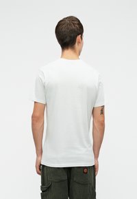 Tricou alb din bumbac cu mânecă scurtă, cu guler clasic rotund, textură netedă și o croială lejeră, purtat cu pantaloni din catifea de măslin.