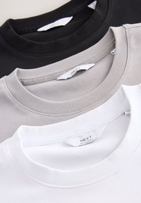 Stapeltje van drie T-shirts met ronde hals in zwart, grijs en wit, elk met een "NEXT Regular Fit" label aan de binnenkant van de kraag.