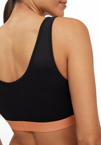 Schwarzer Sport-BH mit einem breiten, pfirsichfarbenen Band am unteren Rand und glattem Material, das ein Racerback-Design und minimale Nähte präsentiert.