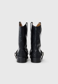 Botas de tobillo de cuero negro con punta afilada, dos bucles laterales y una correa con una hebilla plateada. Suela plana con un acabado suave.