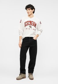 Λευκό πουκάμισο μακρυμάνικο με κόκκινη εκτύπωση "ICECREAM", συνδυασμένο με μαύρο τζιν και μπεζ μπότες. Ευθεία γραμμή, μαλακό ύφασμα και λιτή λεπτομέρεια.