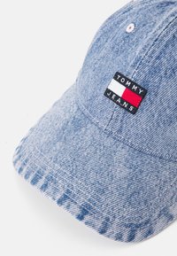 Šviesiai mėlynas džinsinis kepurė su išlenktu kraštu. Yra juodas užrašas su tekstu "TOMMY JEANS" ir raudonais, baltais bei mėlynais akcentais.