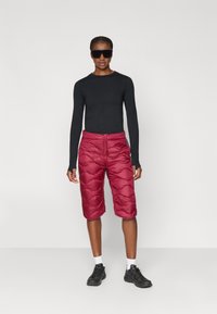 Μαύρη μπλούζα με μακριά μανίκια, μπορντώ επενδεδυμένα σορτς μέχρι το γόνατο, μαύρα γυαλιά ηλίου, λευκές κάλτσες, μαύρα αθλητικά παπούτσια, παρουσιάζοντας έναν εφαρμοστό και κομψό σχεδιασμό.