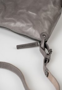 Borsa a tracolla in pelle grigia con chiusura a zip, caratterizzata da una texture liscia, una tracolla regolabile e un'etichetta con il marchio.