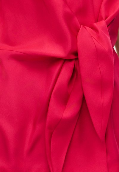 Tissu rouge vif avec un détail de nœud créant des plis et une texture, mettant en valeur un matériau lisse et légèrement brillant.