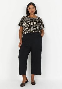 Pantalons cargo noirs raccourcis associés à un haut zèbre beige et noir. L'ensemble présente une coupe décontractée et des manches courtes. Sandales noires en mesh.