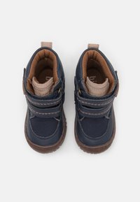 Marineblauwe kinderlaarzen met bruine accenten, klittenbandsluitingen en textiel- en leren materialen. Rond neusontwerp met gevoerde binnenkant.