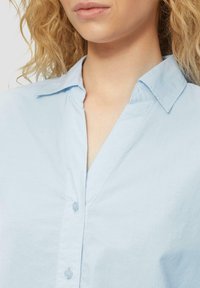 Lichtblauw collared shirt met een knoopsluiting aan de voorkant, een relaxte pasvorm en een zachte textuur met een subtiele glans.