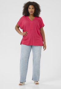 Top rosa con scollo a V, maniche corte e larghe, pannello frontale testurizzato, abbinato a jeans azzurri dritti e sandali bianchi con cinturini.