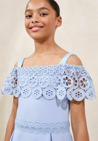 Robe bleu clair avec une superposition en dentelle décorative ornée de motifs floraux, design à épaules dénudées et accents en dentelle assortis à la taille.