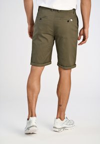 Olijfgroene korte broek met een gestructureerd patroon, opgerolde manchetten en achterzakken; gecombineerd met witte sportschoenen.