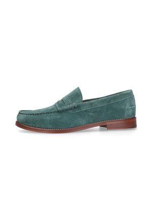 Groene suède herenloafer met pennyriemdetail en bruine lederen zool, profielweergave op witte achtergrond.