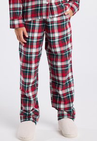 Pijamas de franela en cuadros rojos y verdes, con una parte superior de botones y pantalones holgados, combinados con zapatillas de casa beige de felpa.