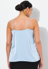 Camiceta azul claro con tirantes delgados ajustables, hecha de un tejido suave y liso. Presenta un escote redondeado y un corte relajado, con dobladillo en la parte inferior.