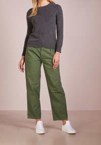 Grå stickad tröja med rund halsringning, parat med gröna vida byxor och vita sneakers, mot en neutral bakgrund.