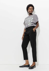 T-shirt graphique gris à manches retroussées, pantalon noir ajusté avec poches latérales, et ballerines noires ornées de pois blancs.