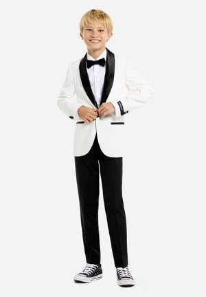 Weißes Smokingjackett mit schwarzen satinbesetzten Revers, schwarze Hose und schwarze Sneakers. Weißes Hemd, schwarze Fliege und kontrastierende Manschettendetails.