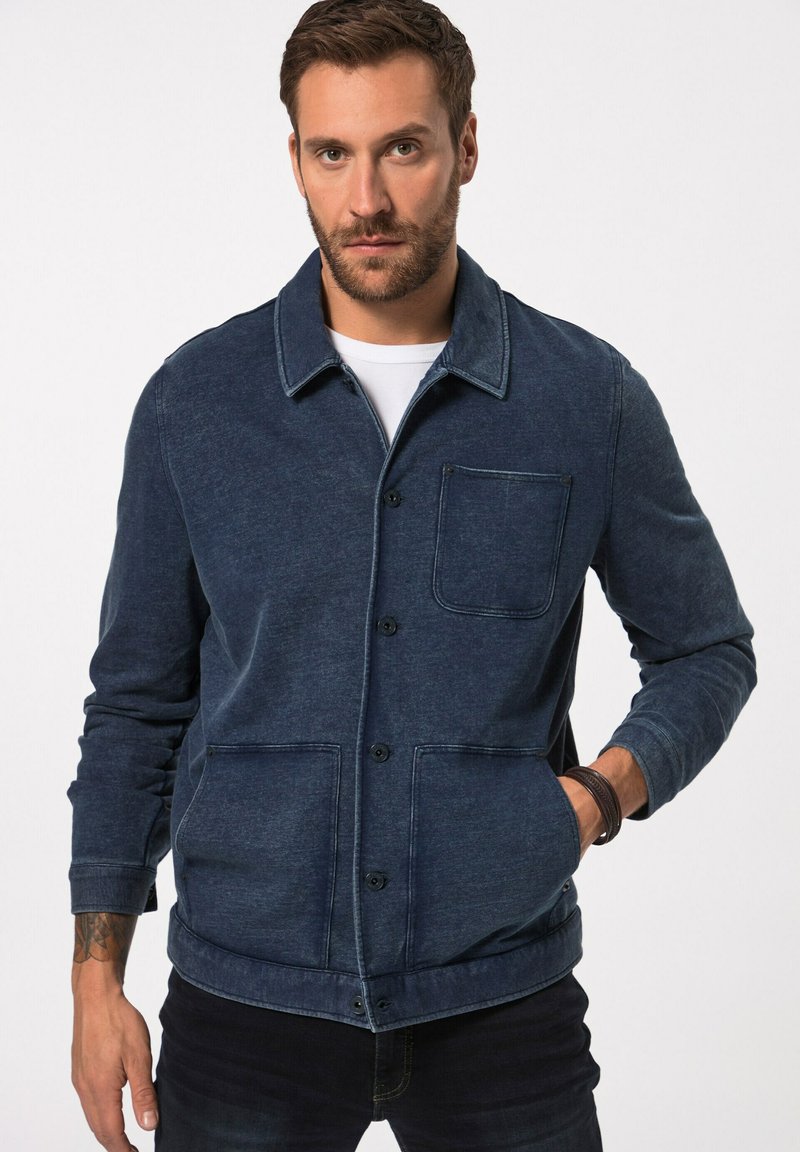 Džínová bunda v tmavě modré barvě s knoflíkovou přední částí, jednou náprsní kapsou a dvěma dolními kapsami. Má volný design a texturovanou tkaninu.