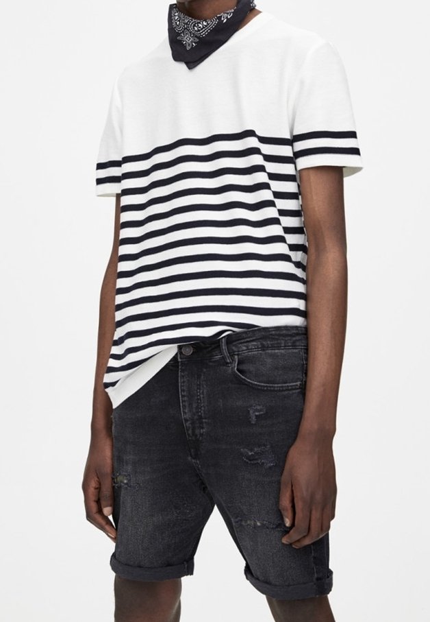 Personne portant un t-shirt à manches courtes rayé blanc et noir, un bandana noir autour du cou et un short en denim noir retroussé avec des détails usés.