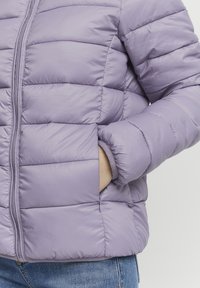 Jasnofioletowa puchowa kurtka z pikowanym wzorem, widocznymi szwami i bocznymi kieszeniami. Gładka faktura i stójka. Zapięcie na suwak.