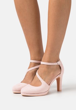 Chaussures à talons hauts en suede rose avec une bride au cheville, présentant un bout arrondi et un talon bloc solide. Texture lisse avec une finition douce.