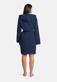Accappatoio blu navy con cappuccio, maniche lunghe e cintura. Tessuto morbido, taglio fino al ginocchio, texture liscia, dettagli minimi.