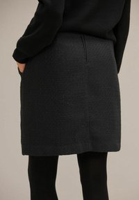 Svart texturerad kjol med rak skärning, sömdetaljer bak och sidofickor. Matchad med svarta strumpbyxor för en monokromatisk look.