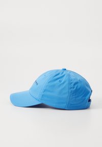 Blue cotton baseball cap with a curved brim, adjustable strap, and embroidered text on the front. Features stitching details and ventilation holes.