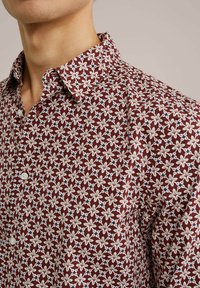 Rood bloemenpatroon shirt met een button-down kraag en witte bloemenontwerpen met donkere accenten, gemaakt van lichtgewicht stof.