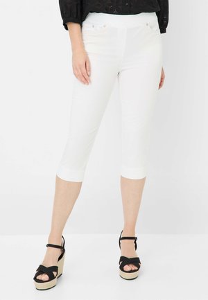 Pantalons capri blancs avec une coupe slim, présentant une texture lisse, deux poches avant et un ourlet fini. Associés à des sandales à talons compensés noires à lanières.