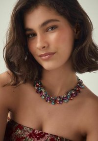 Farbige Statement-Halskette mit verschiedenen geformten Edelsteinen in Rot, Blau, Grün und Lila, auf einer Metallkette montiert.
