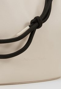Sac beige avec fermeture cordon noué noire et logo discrètement embossé « Fritzi aus Preußen » sur une surface en cuir lisse.