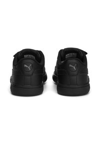 Baskets noires en cuir avec une texture lisse, un collier rembourré et une semelle en caoutchouc. Présence d'un logo sur le talon et la languette. Design minimaliste.