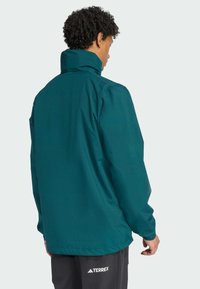 Veste imperméable teal avec col haut, manches longues et coupe décontractée. Comprend des poignets élastiques et un détail de logo à l'ourlet.