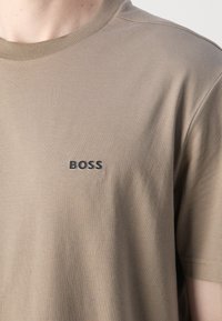 Kortermet beige t-skjorte laget av glatt bomull, med en svart "BOSS"-logo på brystet, rund halsutskjæring og normal passform.