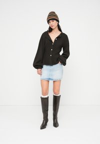 Καφέ πλεκτή ζακέτα με μεγάλα κουμπιά, φούστα μίνι από ανοιχτό μπλε τζιν, ψηλές σκούρες καφέ μπότες και πολύχρωμο ριγέ πλεκτό σκουφάκι.