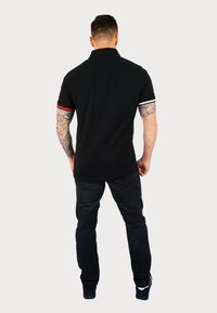 Svart pikétröja med korta ärmar som har röda och vita detaljer. Bärs med svarta byxor. Designen är enkel med en klassisk krage.