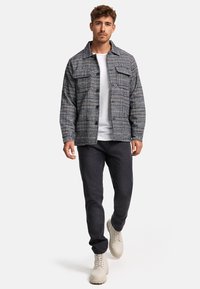 Checkered jacket in gray and black, featuring two chest pockets, paired with a white t-shirt and dark jeans, accented by beige boots.