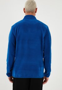 Blaue Fleecejacke mit Kragen, langen Ärmeln und glatter Textur. Hat ein einfaches Design ohne sichtbare Beschläge oder Muster.