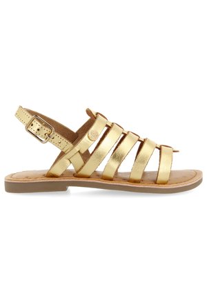 Gouden metalen sandalen met platte zool, verstelbare enkelriem en een zachte binnenvoering. Voorzien van meerdere platte bandjes over de voet.