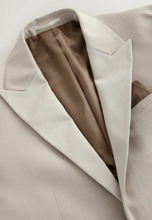 Sacou bej cu un exterior texturat și o căptușeală netedă de culoare maro. Dispune de un rever cu colțuri și o batistă în buzunarul de la piept.