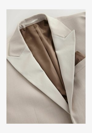 Veste de costume beige avec un extérieur texturé et une doublure en satin marron. Présente un revers cranté et un mouchoir de poche dans la poche poitrine.