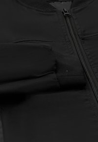 Fekete bomberdzseki cipzáras záródással, bordázott mandzsettákkal és sima, matt anyaggal. Nincsenek látható minták vagy díszítések.